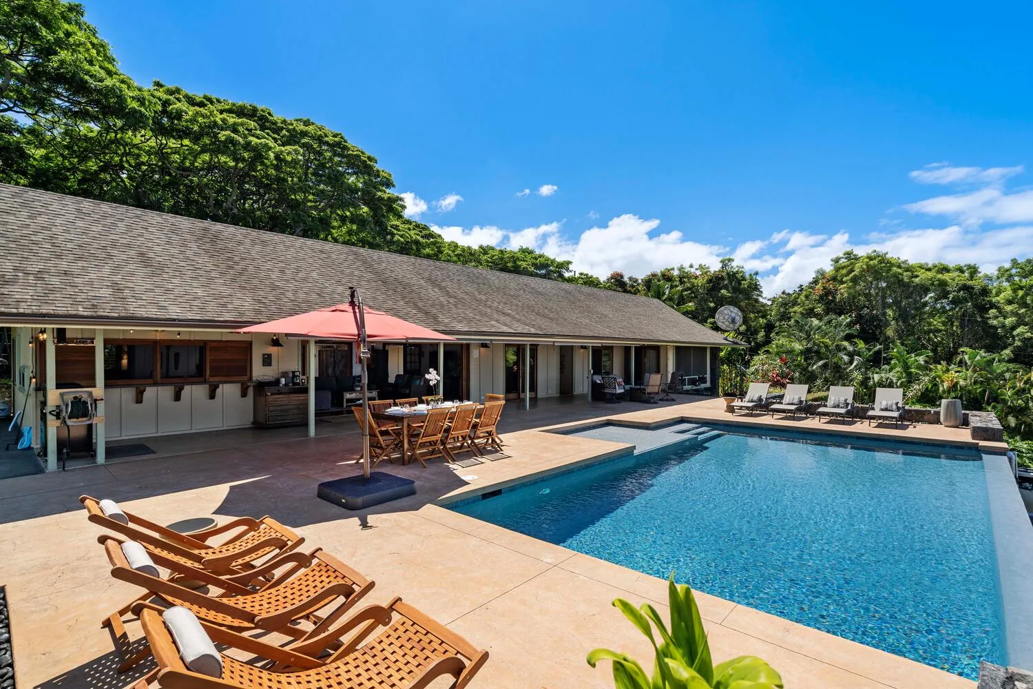 Una piscina junto a un patio con asientos al aire libre y una mesa de comedor.