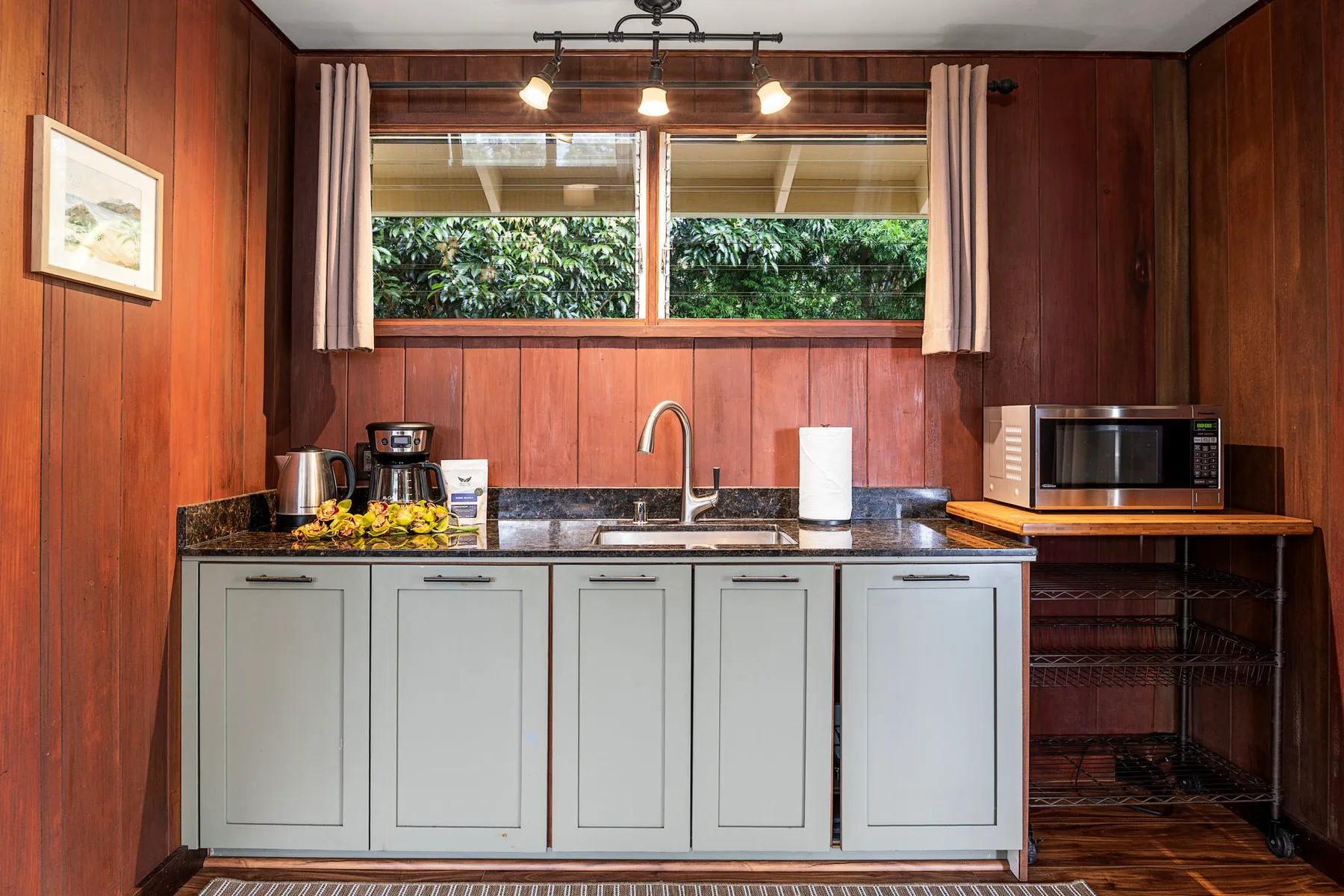 Una cocina compacta con gabinetes claros, un fregadero y una ventana con vista a la vegetación.