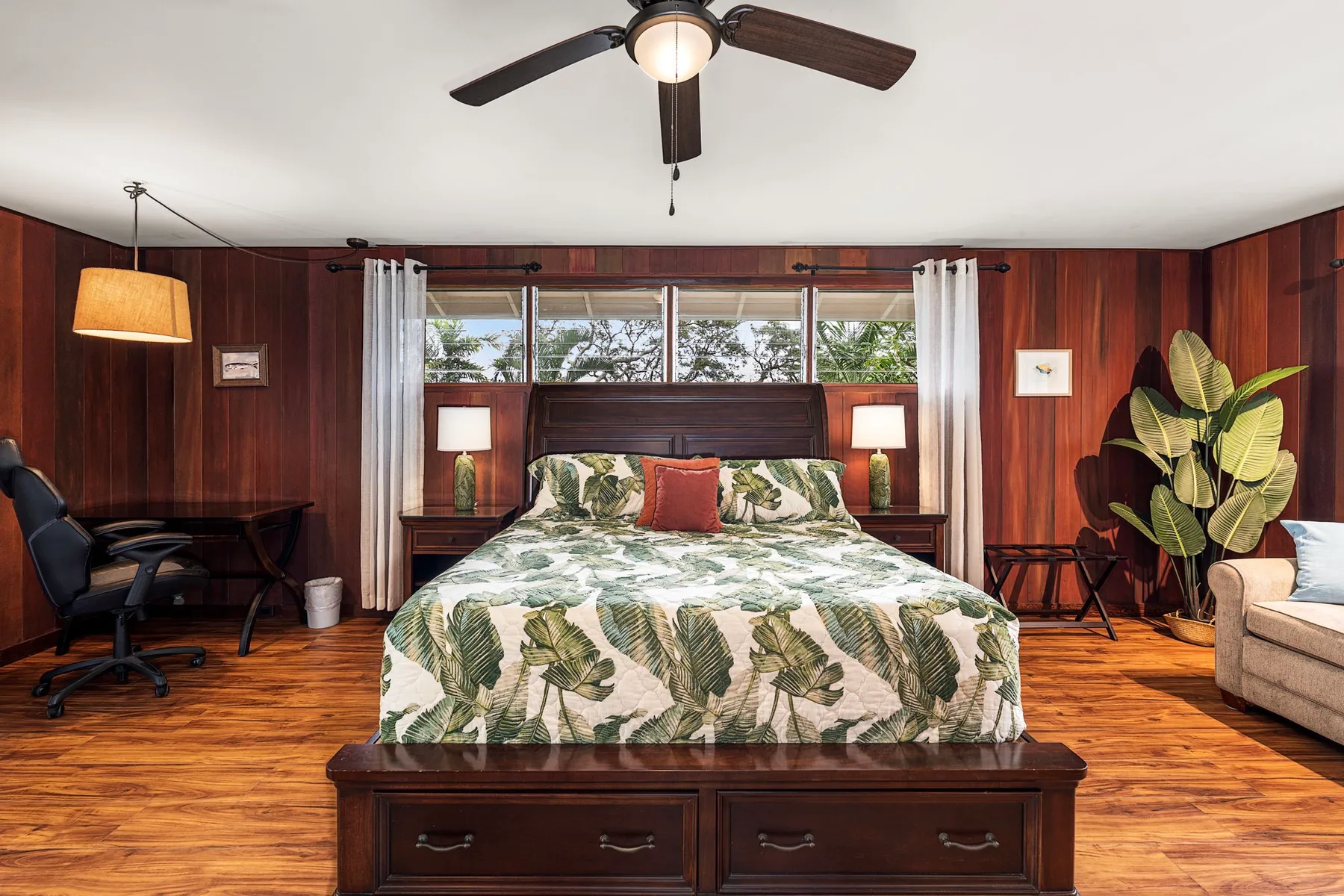 Un dormitorio con una cama grande bajo una ventana y paredes revestidas de madera oscura.