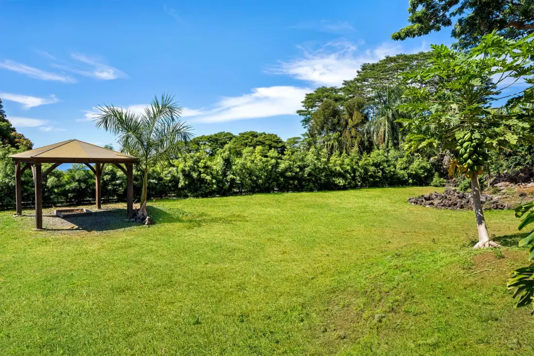 Un jardín con césped, una glorieta sombreada y árboles frondosos.