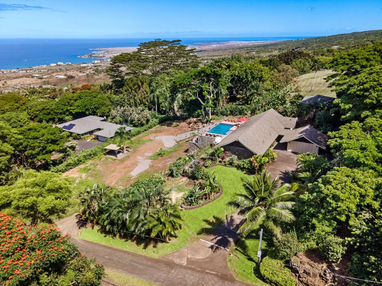 Una vista aérea muestra edificios, una piscina y jardines tropicales cerca de la costa.