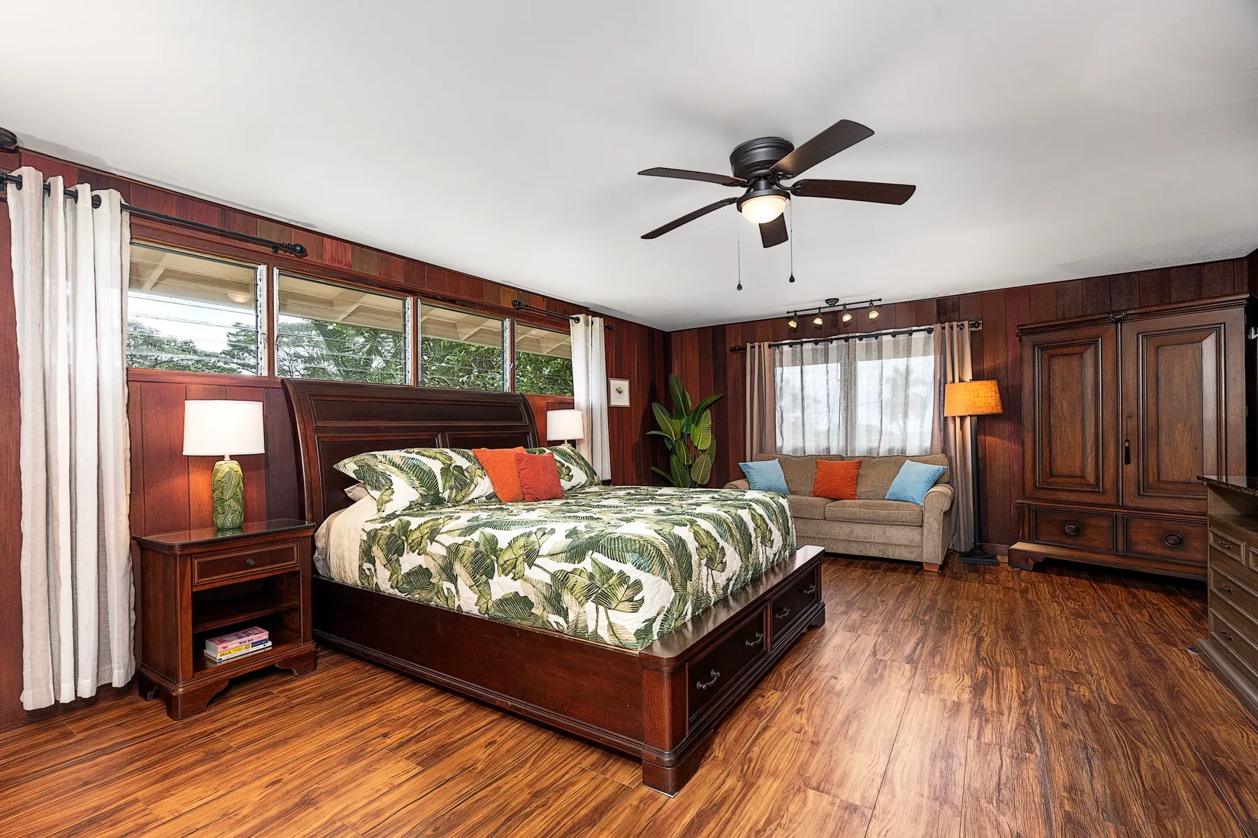 Un dormitorio con una cama grande y una zona de estar junto a las ventanas.