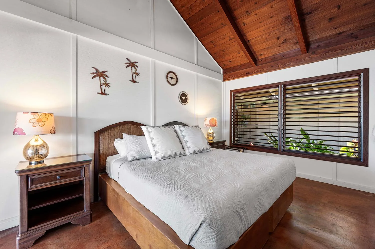 Un dormitorio con cama, mesas de noche y ventanas bajo un techo revestido de madera.