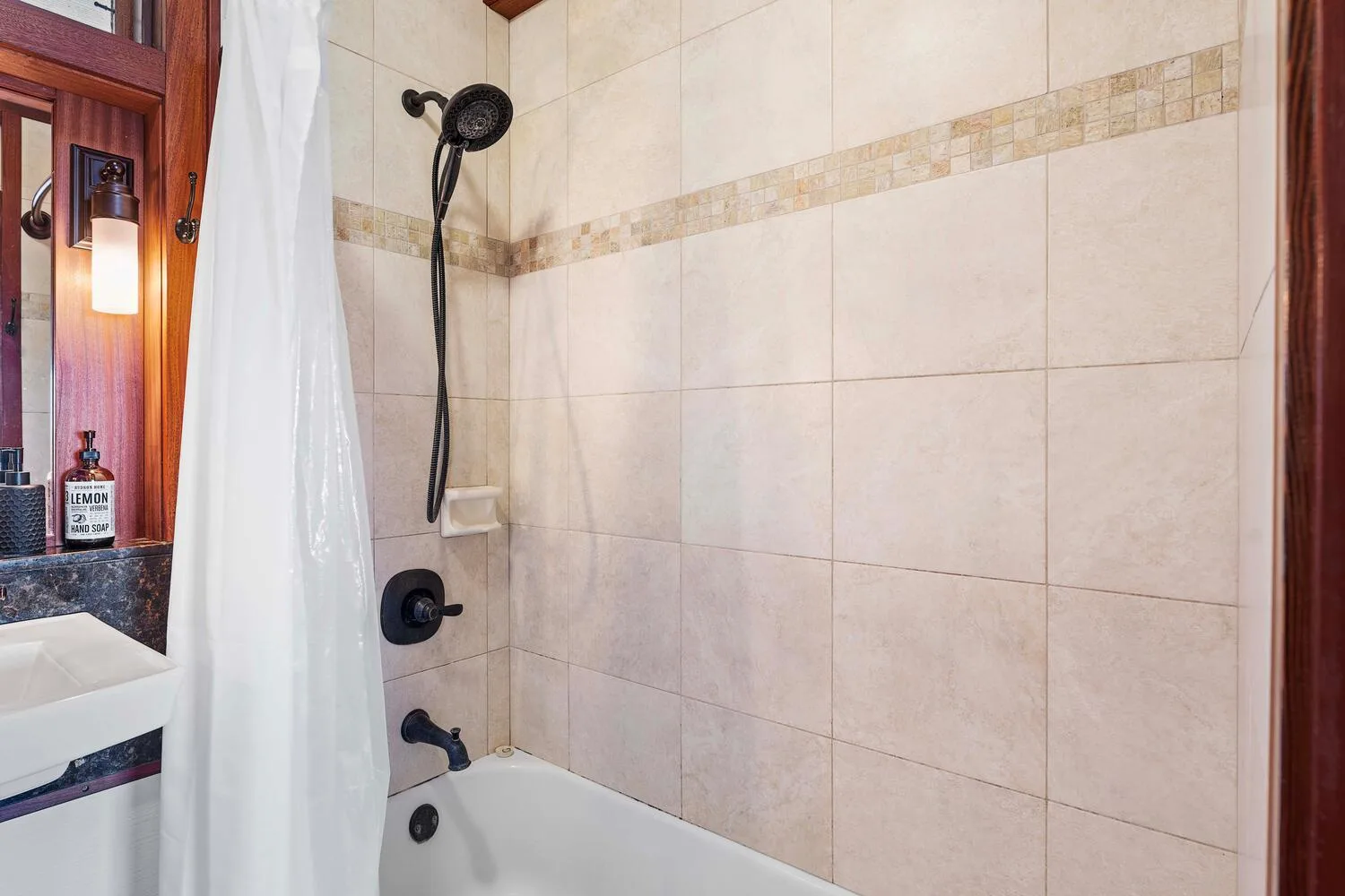Un baño alicatado con bañera, cabezal de ducha y cortina blanca.