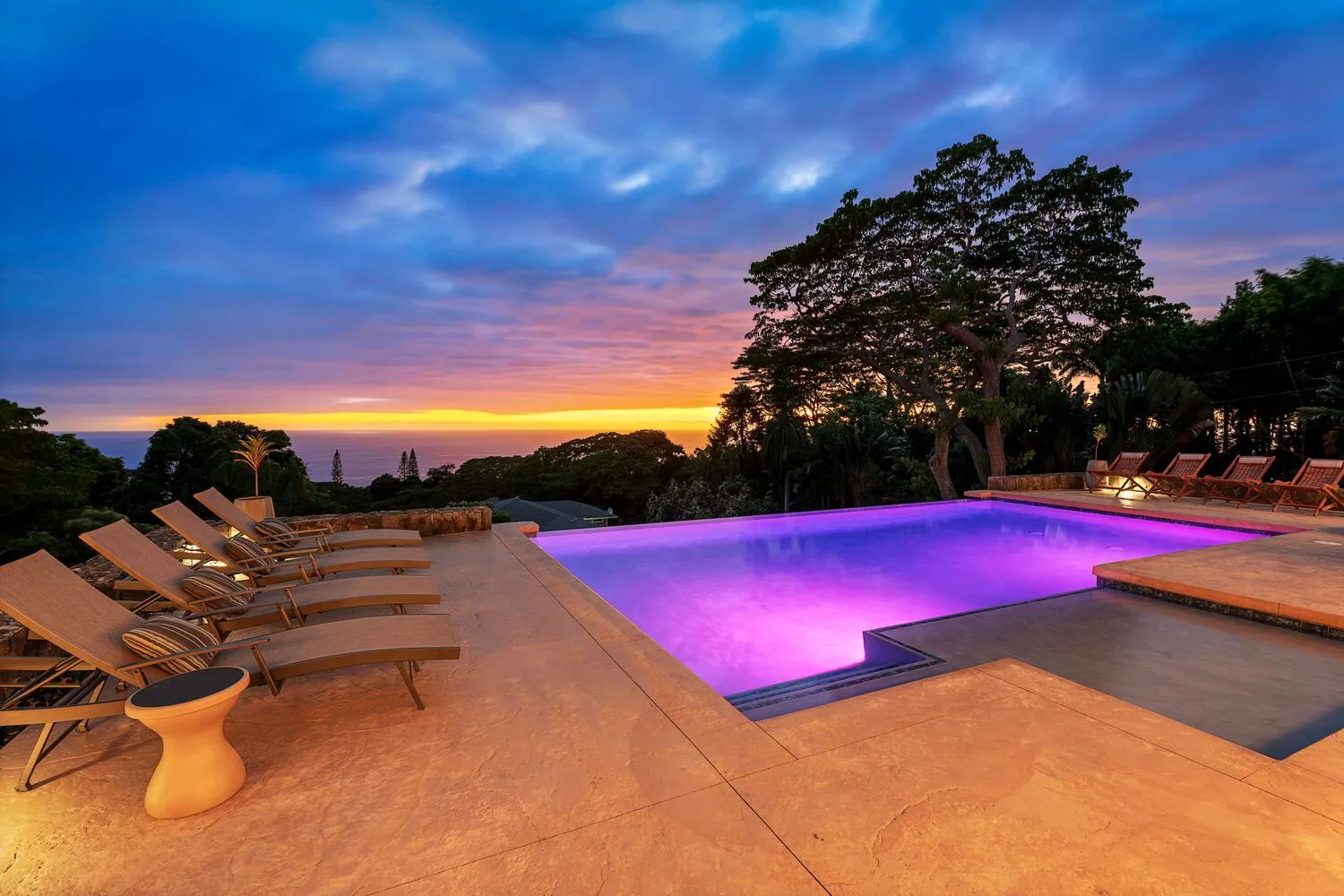 La piscina exterior y la zona de descanso miran hacia los árboles bajo un cielo de atardecer colorido.