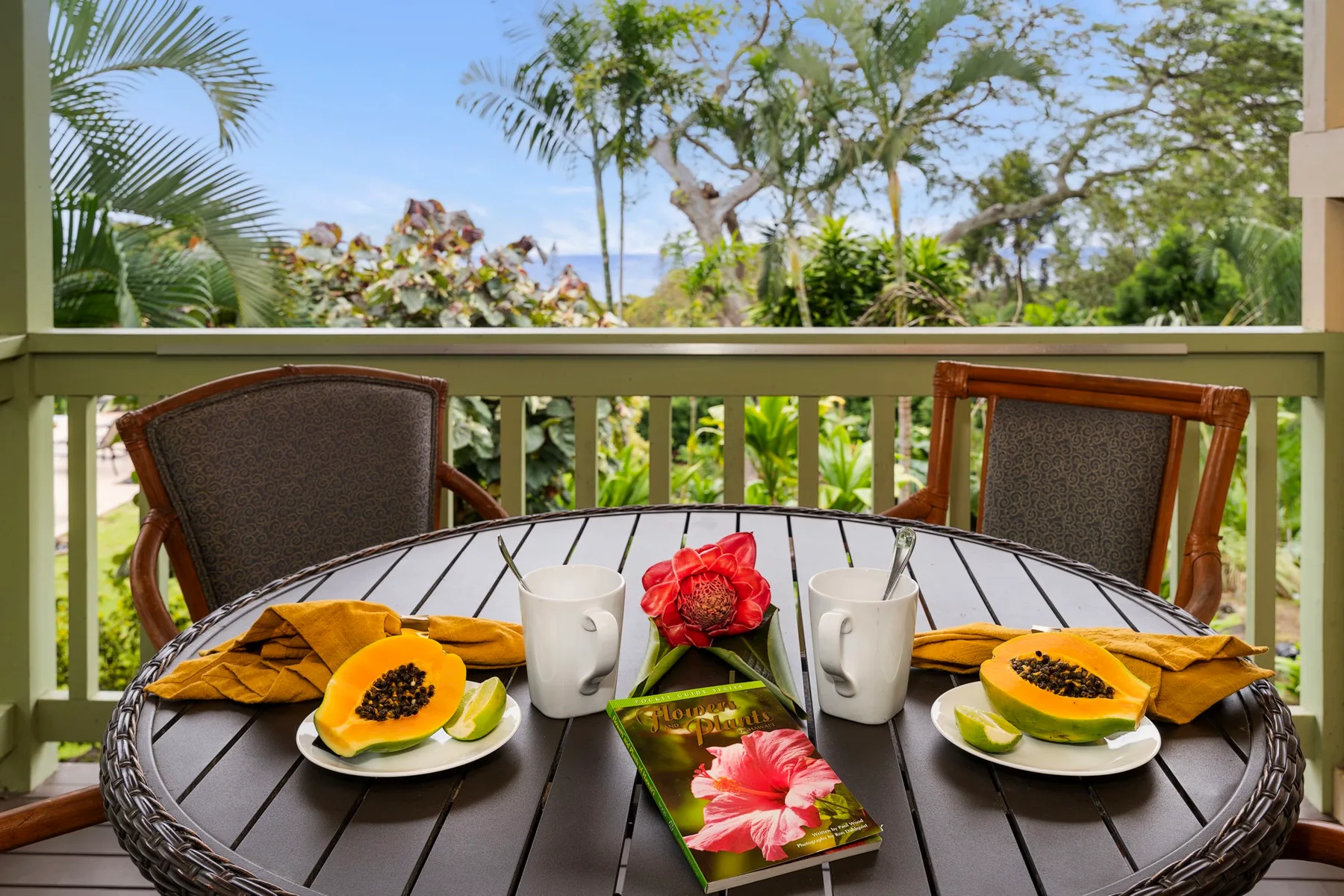 Una mesa de patio con fruta y flores está junto a una barandilla exterior.