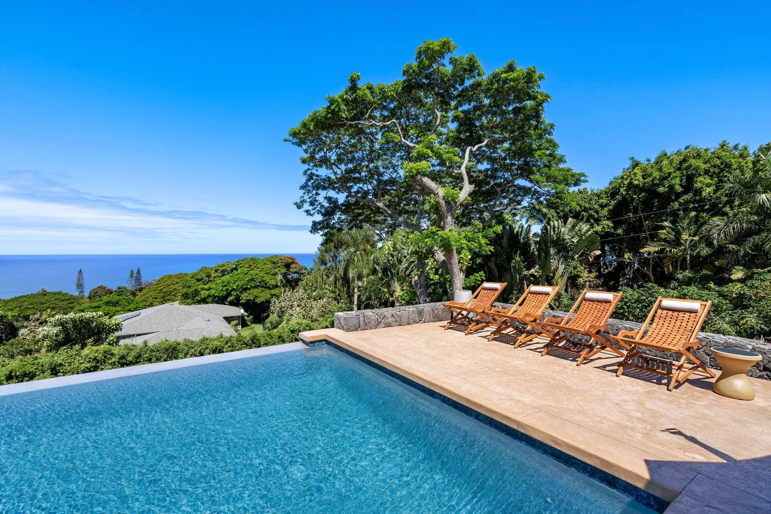 Una piscina al aire libre junto a una terraza de madera con tumbonas y vistas al mar.