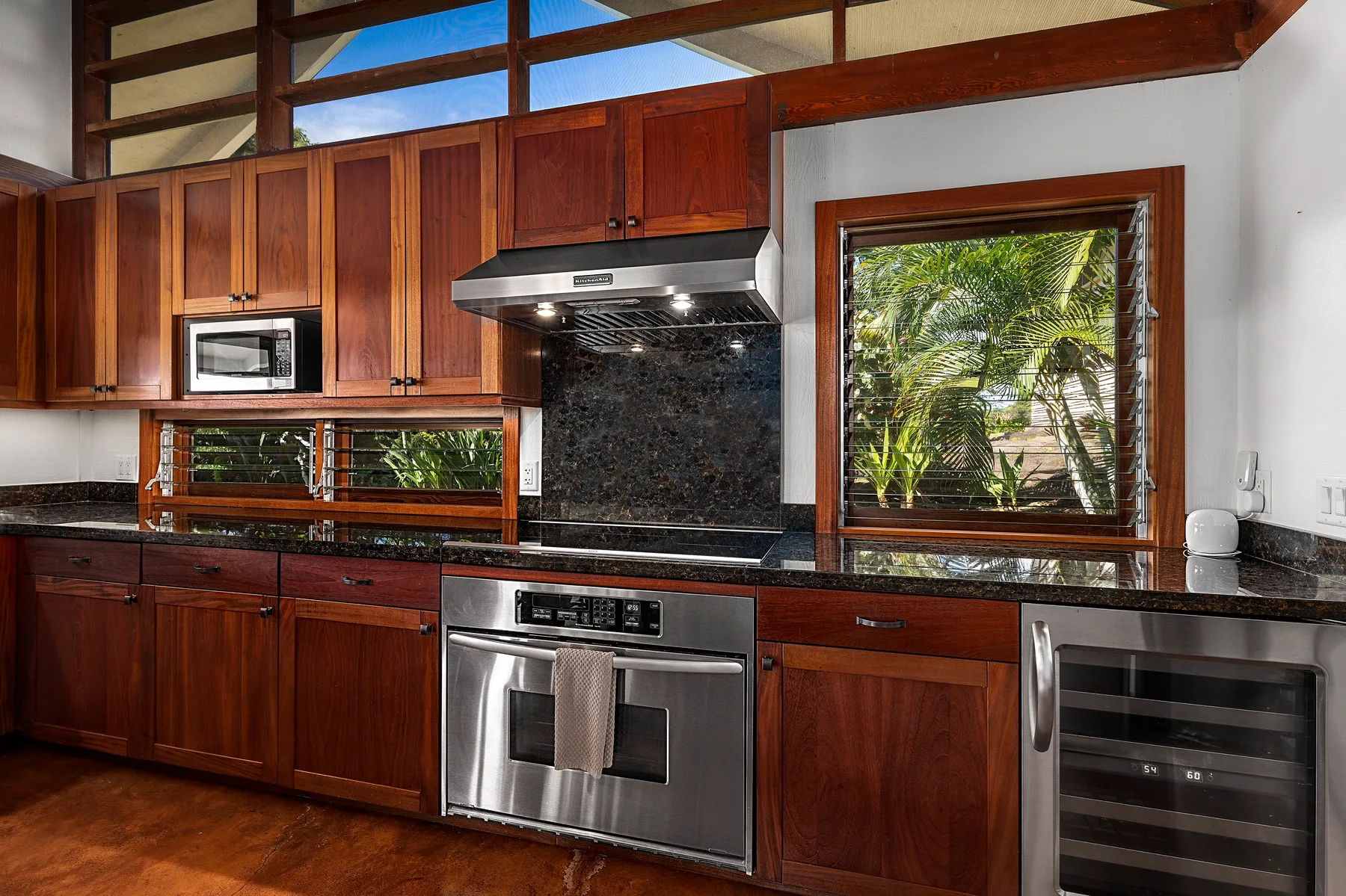 Una cocina con gabinetes de madera oscura, electrodomésticos de acero inoxidable y ventanas con vista a la vegetación.