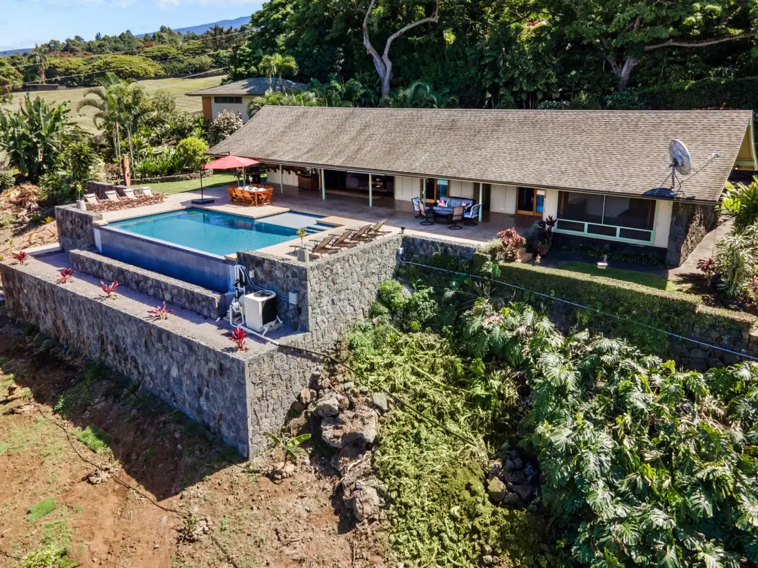 Una casa en una ladera con piscina y vegetación alrededor.