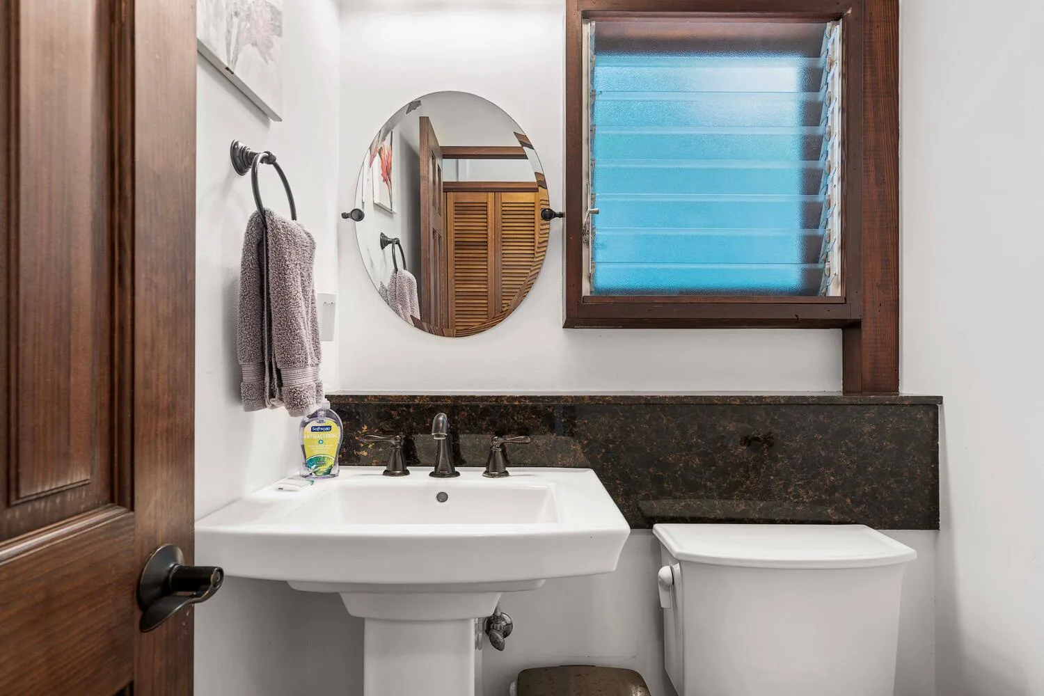 Un baño con lavabo, inodoro y espejo redondo en la pared.
