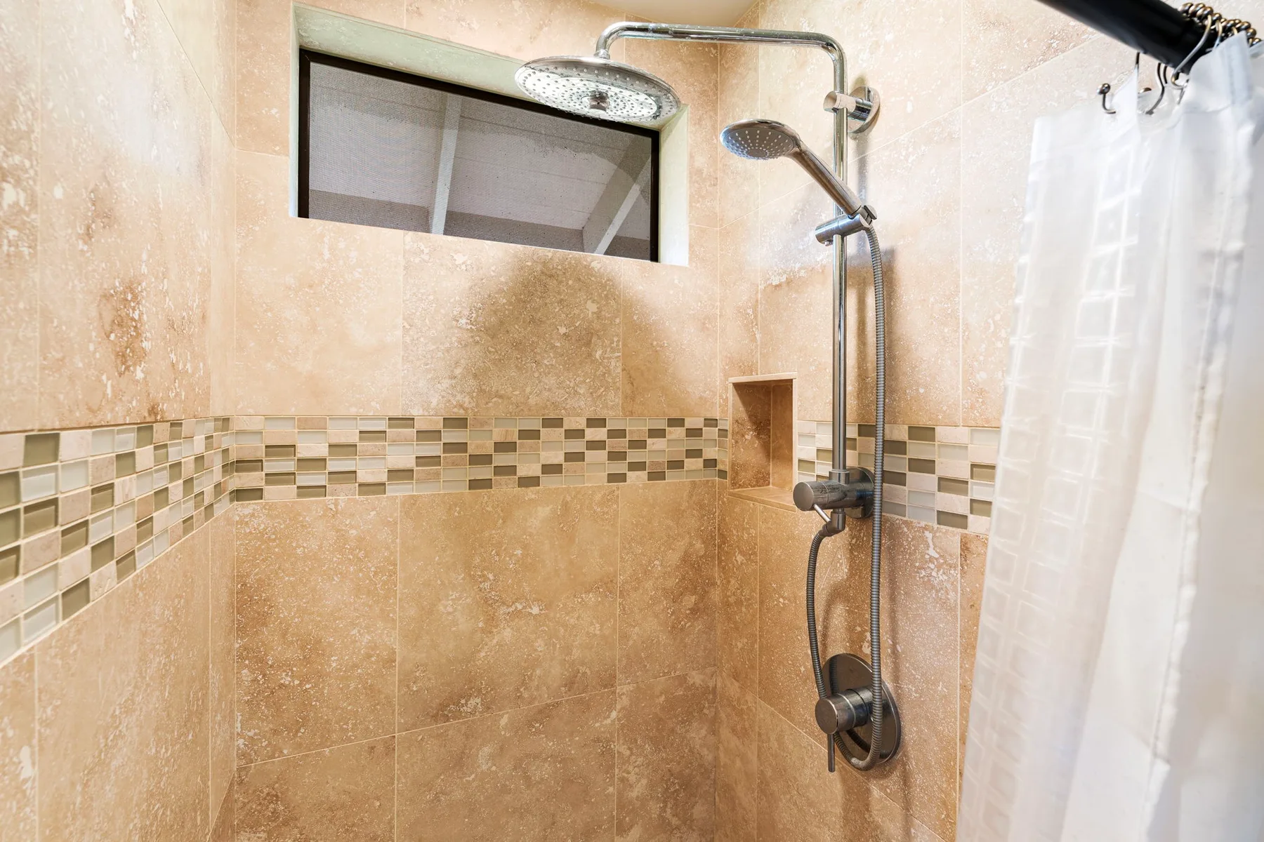 Una ducha con azulejos, una ducha de mano y una cortina blanca.