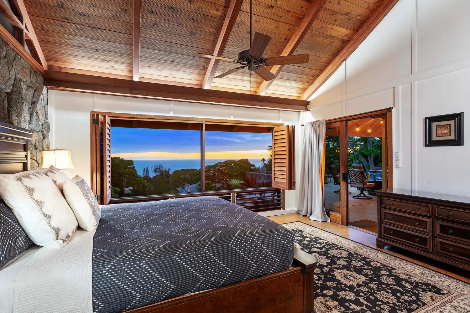 Un dormitorio con una cama grande, techo de madera y amplias ventanas con vista a los árboles.