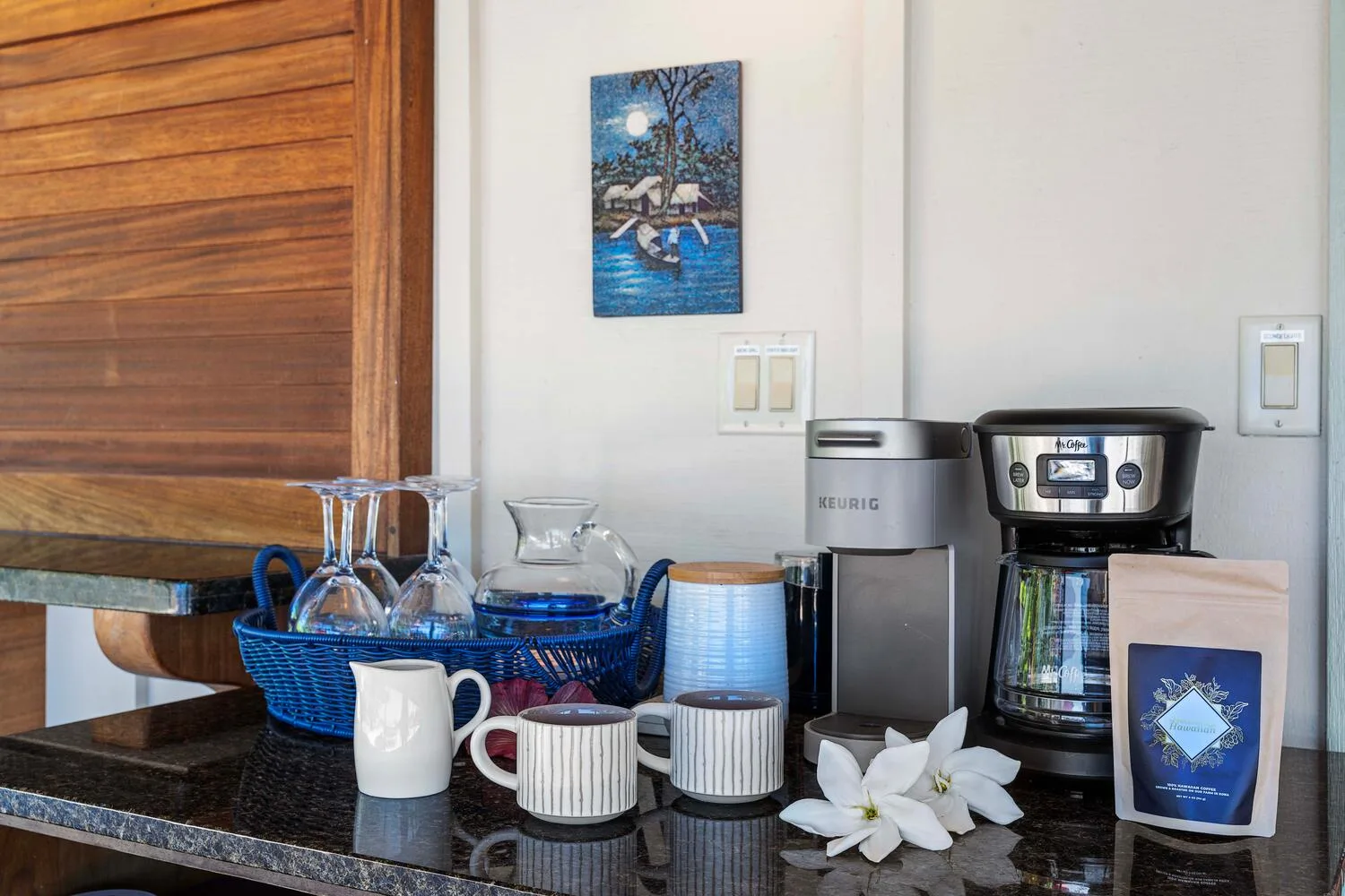 Una estación de café está sobre una encimera, con cafetera, tazas y artículos para servir.