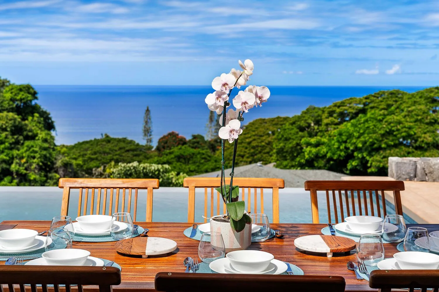 Una mesa al aire libre está puesta con vajilla y flores frente al mar.