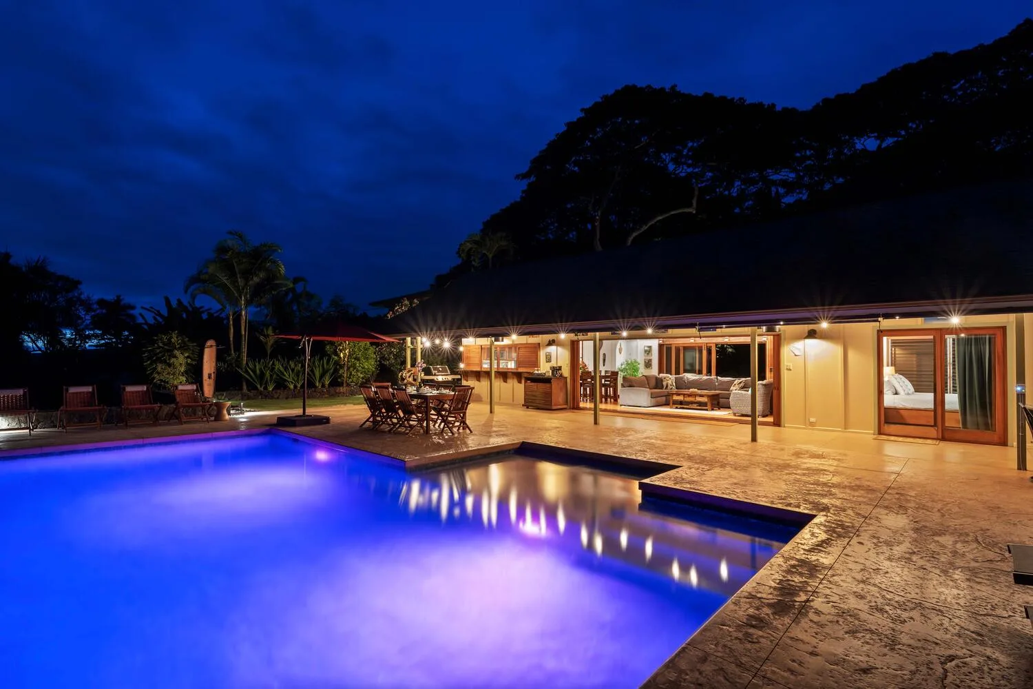 Una piscina iluminada junto a una casa cálidamente iluminada por la noche.