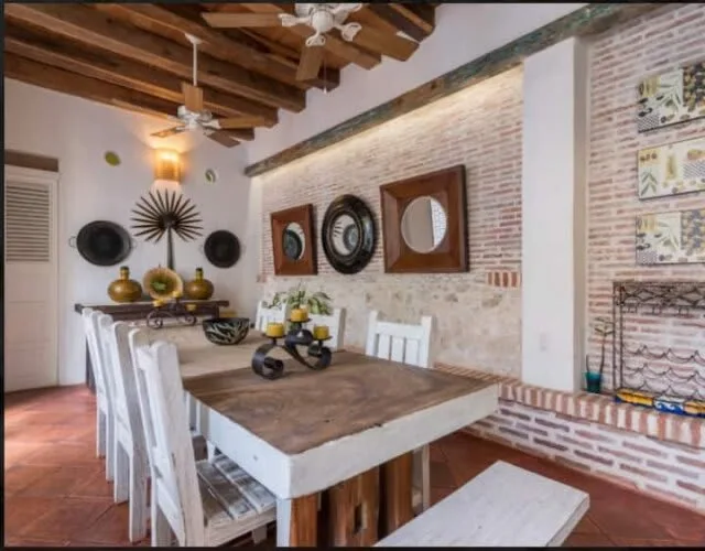 A dining area with a long table, white seating, and decorative wall pieces.