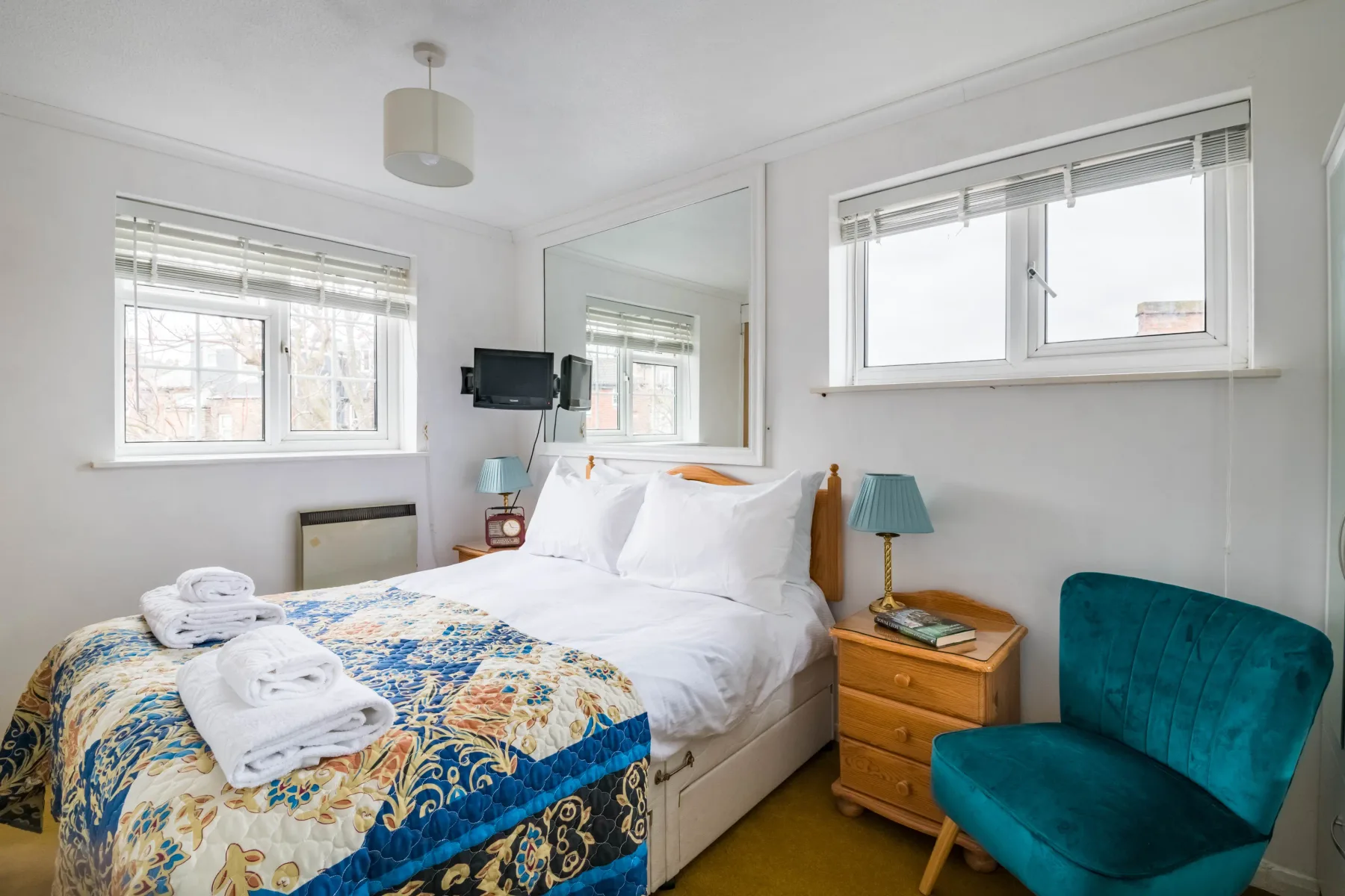 Un dormitorio luminoso con una cama doble y un sillón verde azulado junto a la ventana.