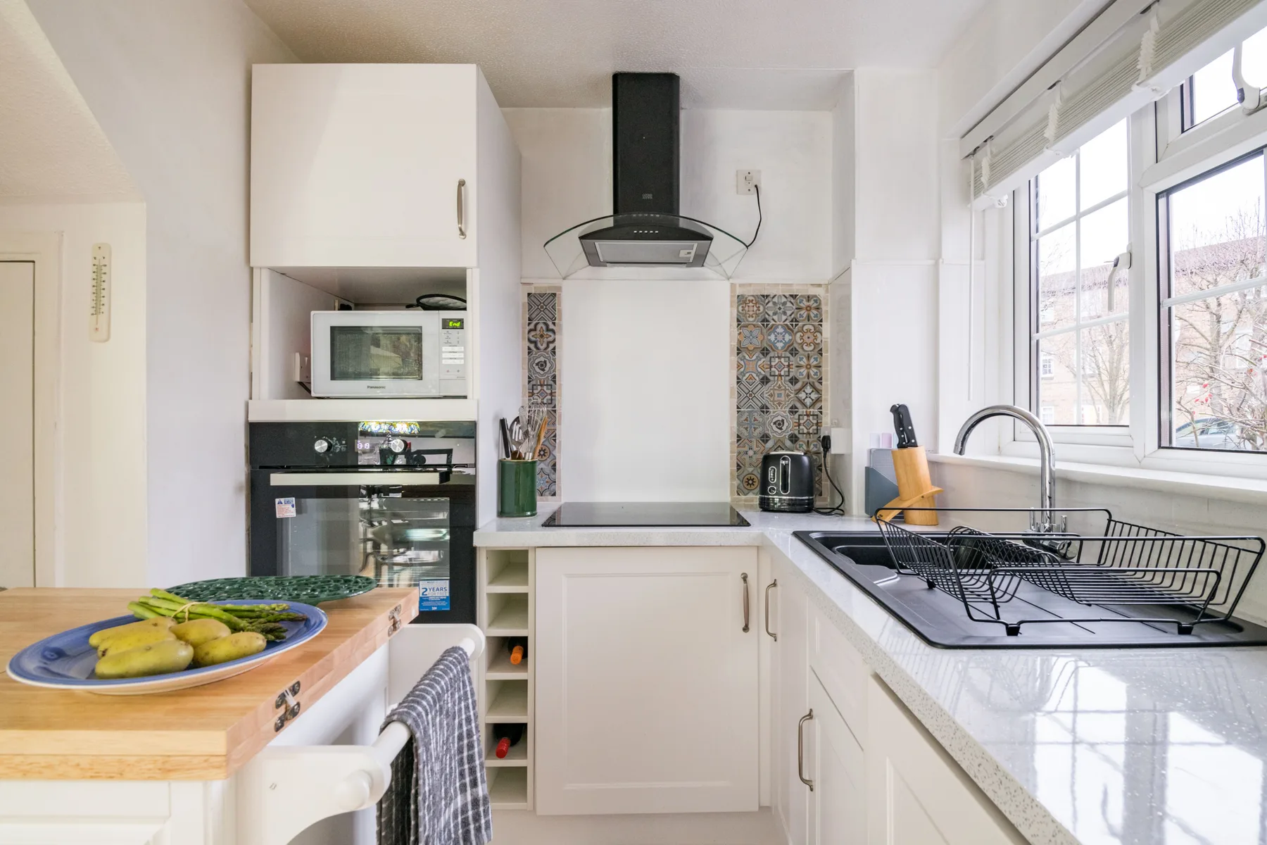 Una cocina luminosa con gabinetes blancos, electrodomésticos empotrados y una ventana grande.