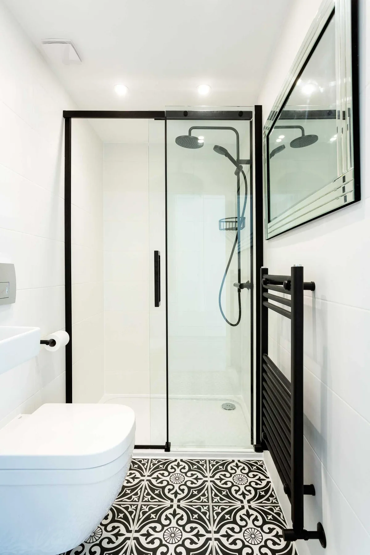 Un baño luminoso con una ducha de cristal y suelo de baldosas estampadas.