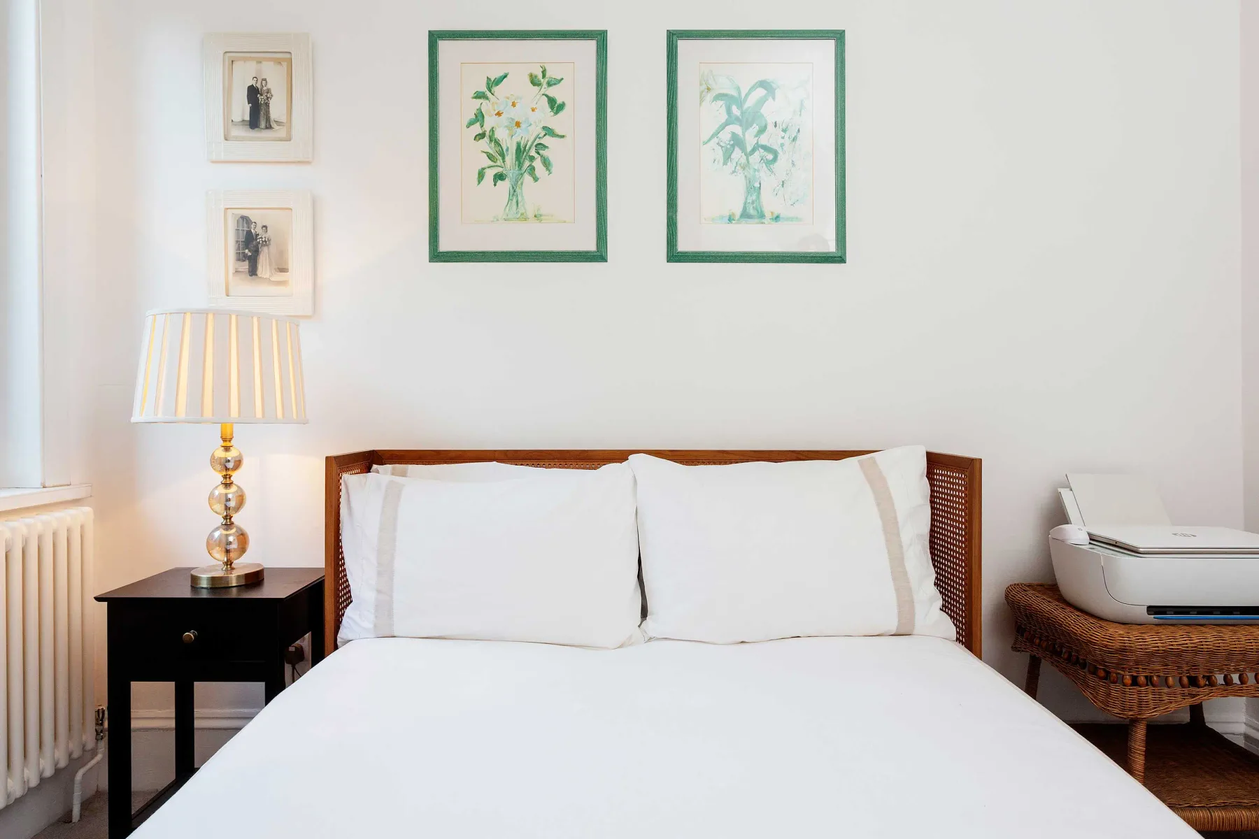 Un dormitorio con una cama bien tendida y láminas botánicas enmarcadas.