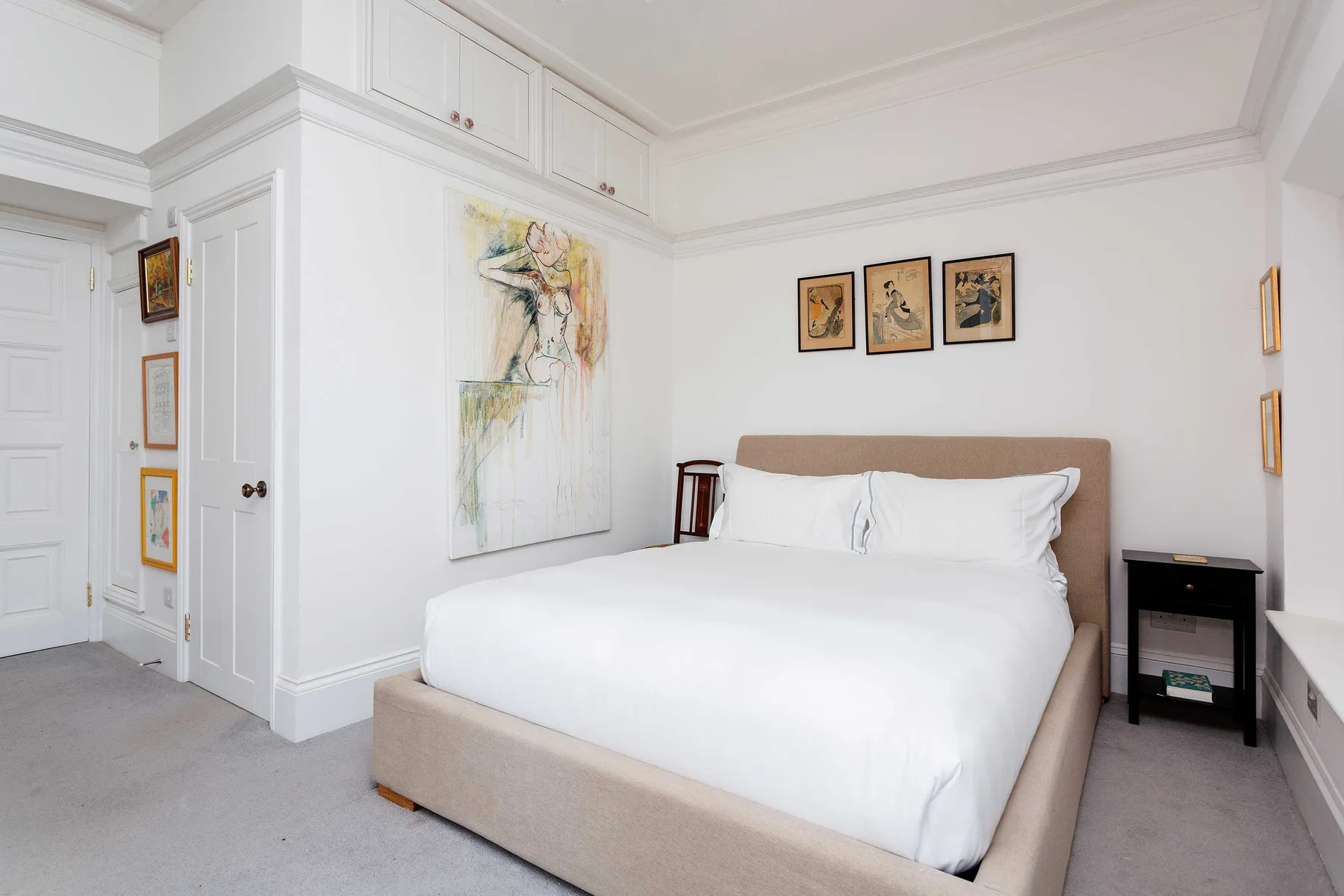 Un dormitorio luminoso tiene una cama grande bajo cuadros enmarcados.