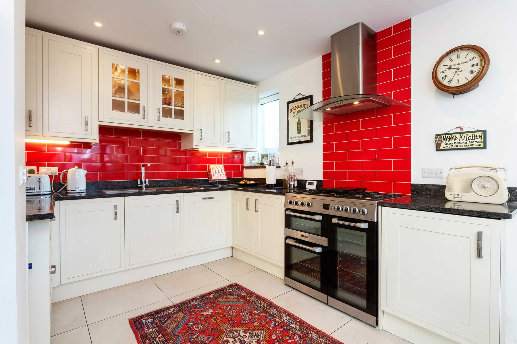 Una cocina luminosa con gabinetes blancos, azulejos rojos y una estufa central.