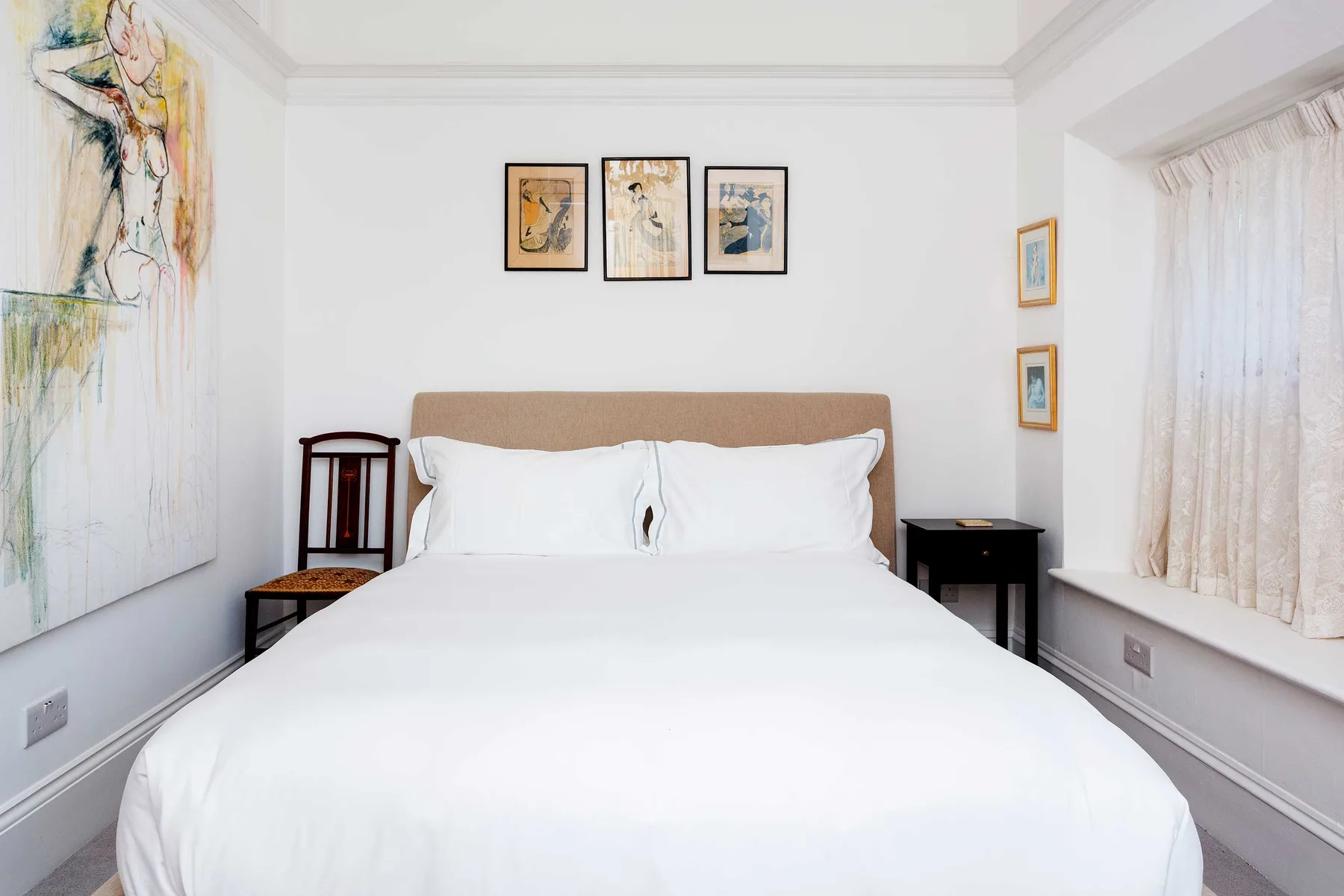 Un dormitorio con una cama bien tendida y cuadros enmarcados en la pared.