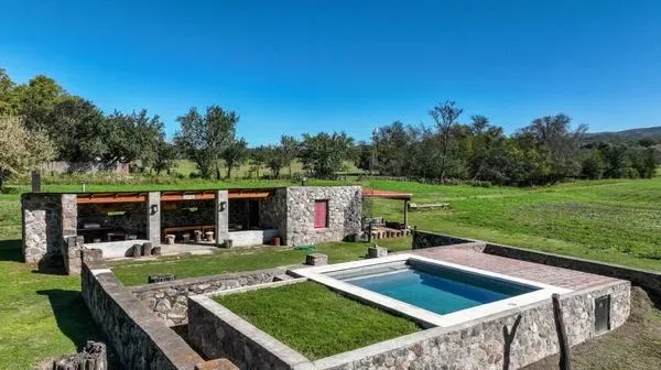 Un patio exterior de piedra rodea una piscina rectangular junto a un edificio bajo de piedra.