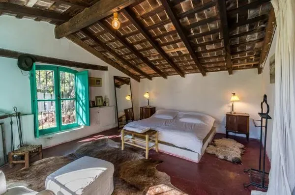 Un dormitorio con una cama bajo un techo oscuro de vigas expuestas y junto a una ventana de marco verde.