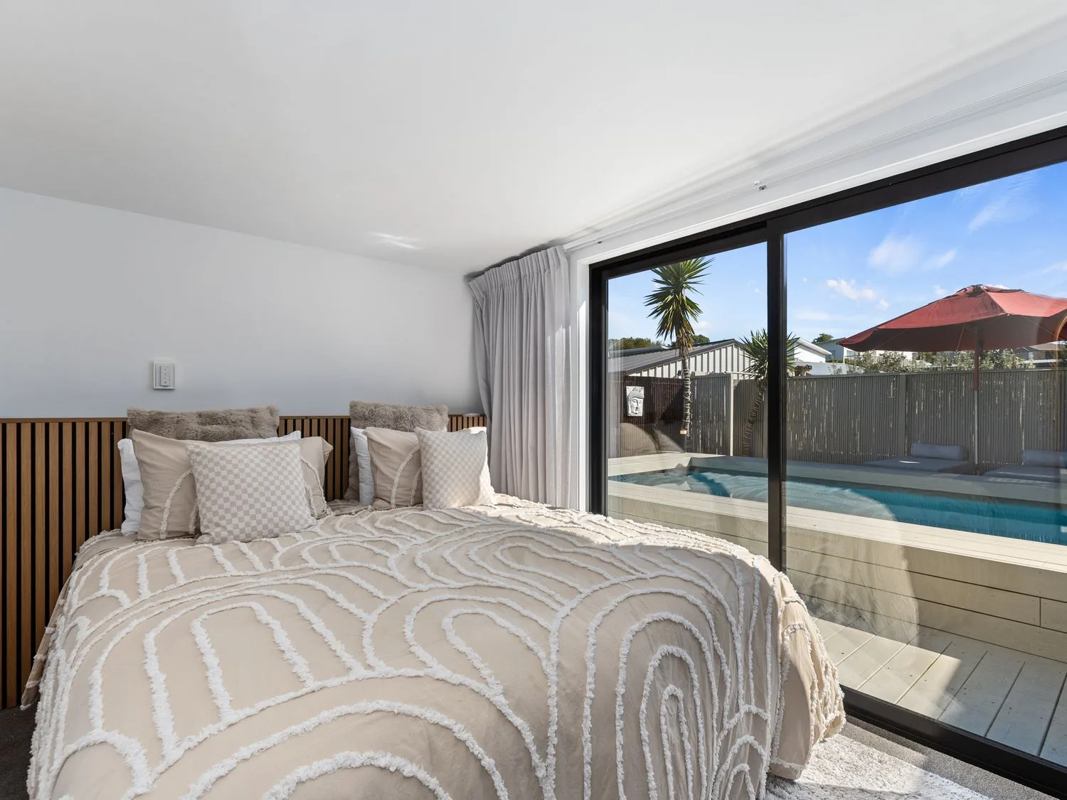 Un dormitorio con una cama y una ventana con vistas a una piscina en Sun Kissed Pool Villa - Mangawhai Heads