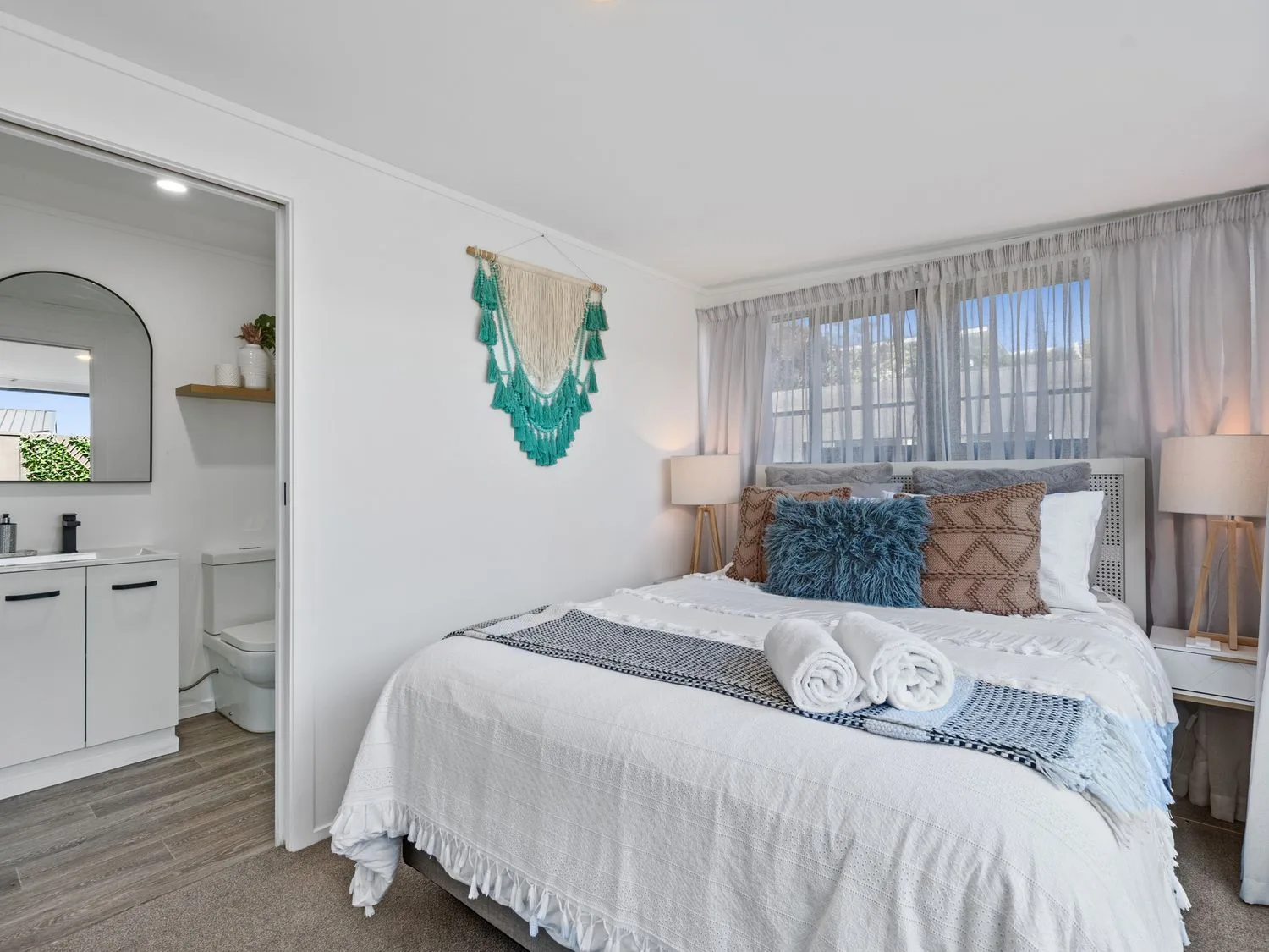 Un dormitorio con una cama, mesas de noche y un baño contiguo en Sun Kissed Pool Villa - Mangawhai Heads