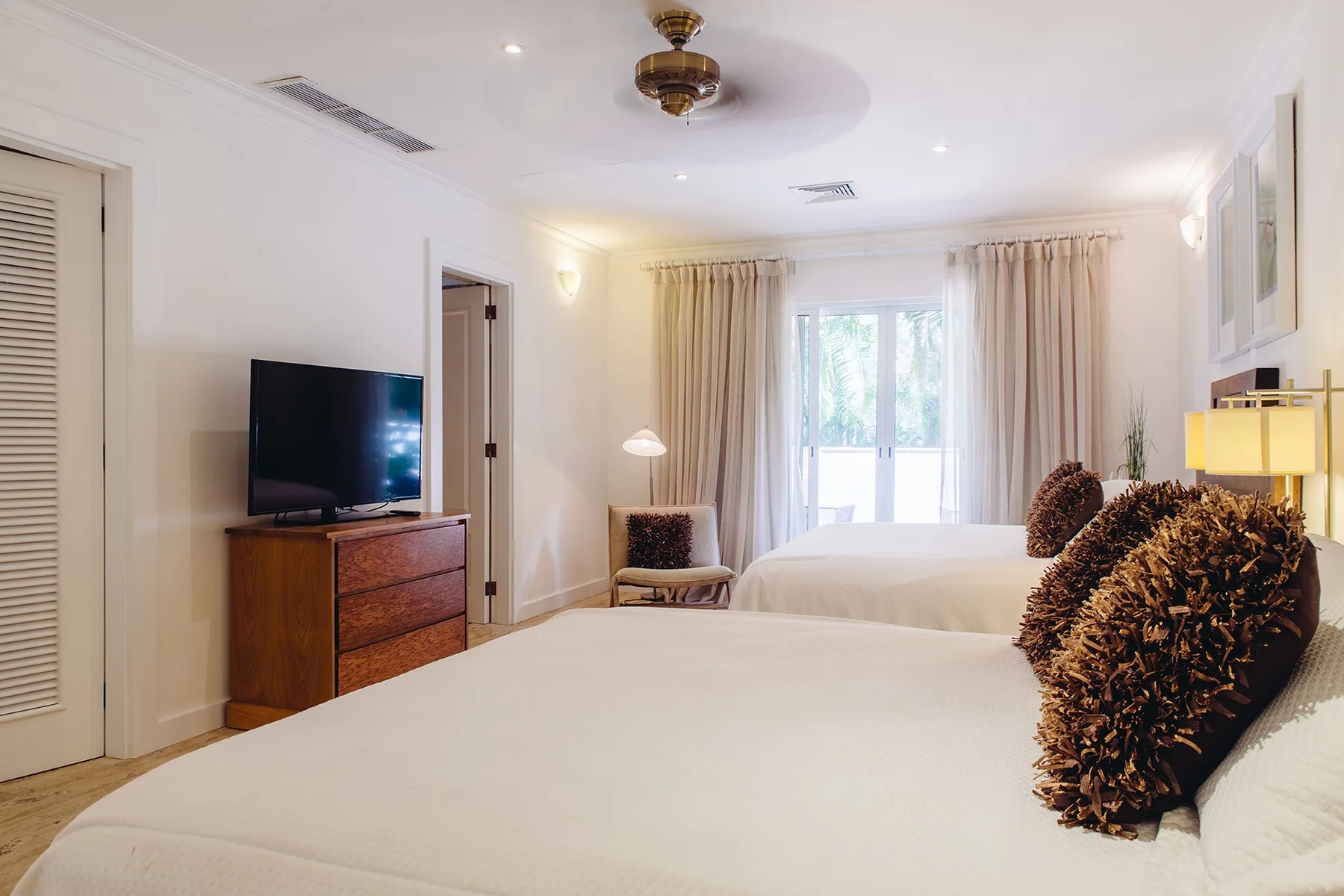 Un dormitorio con dos camas, un televisor y cortinas alrededor de una ventana luminosa.