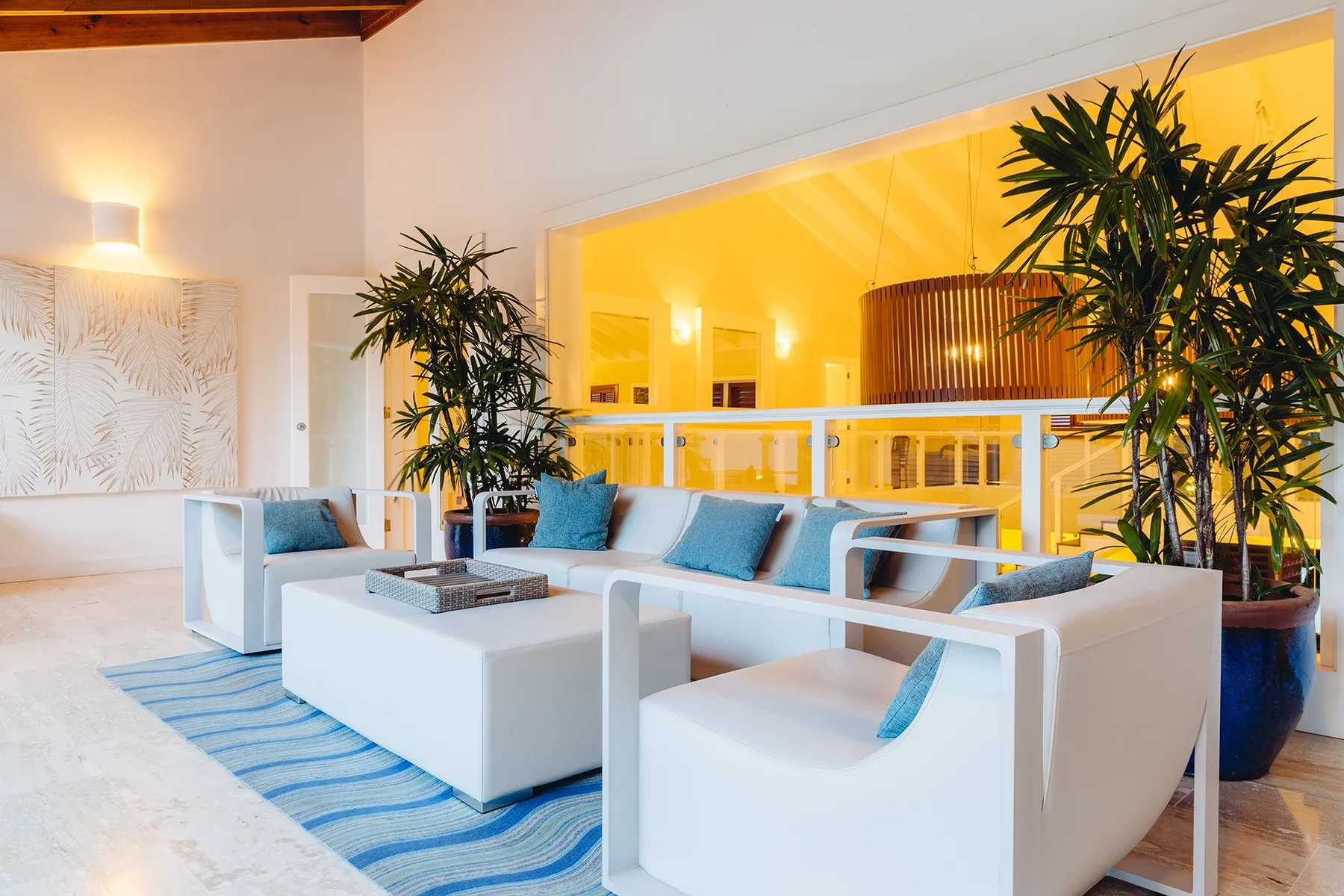 Una sala luminosa con asientos blancos, una mesa baja y plantas frondosas.