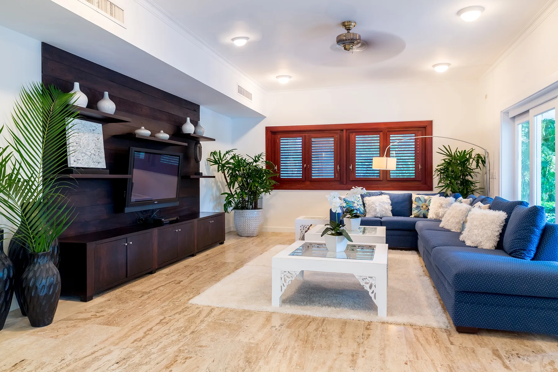 Una sala luminosa con asientos azules, una mesa de centro blanca y un televisor montado en la pared.