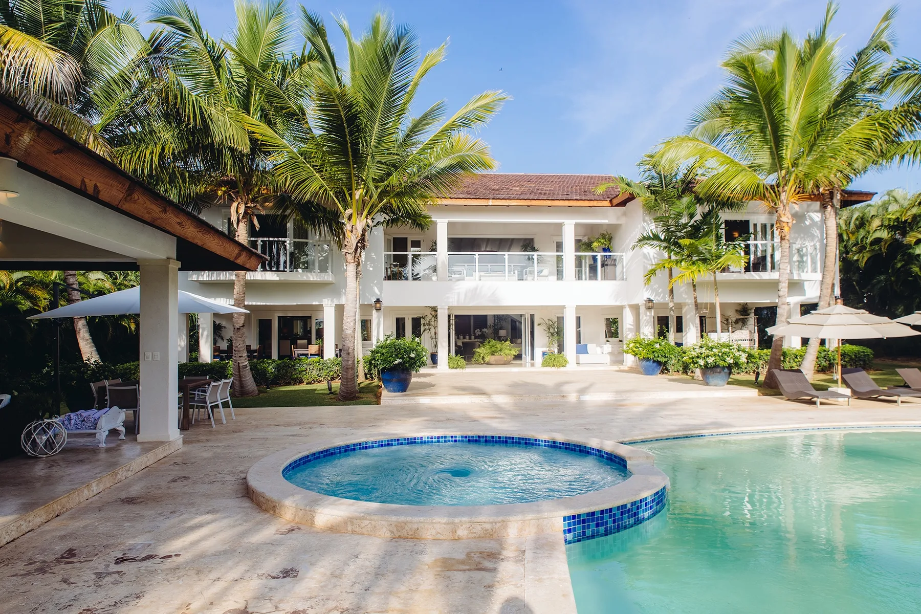 Un patio tropical con una piscina frente a un edificio blanco de dos plantas.