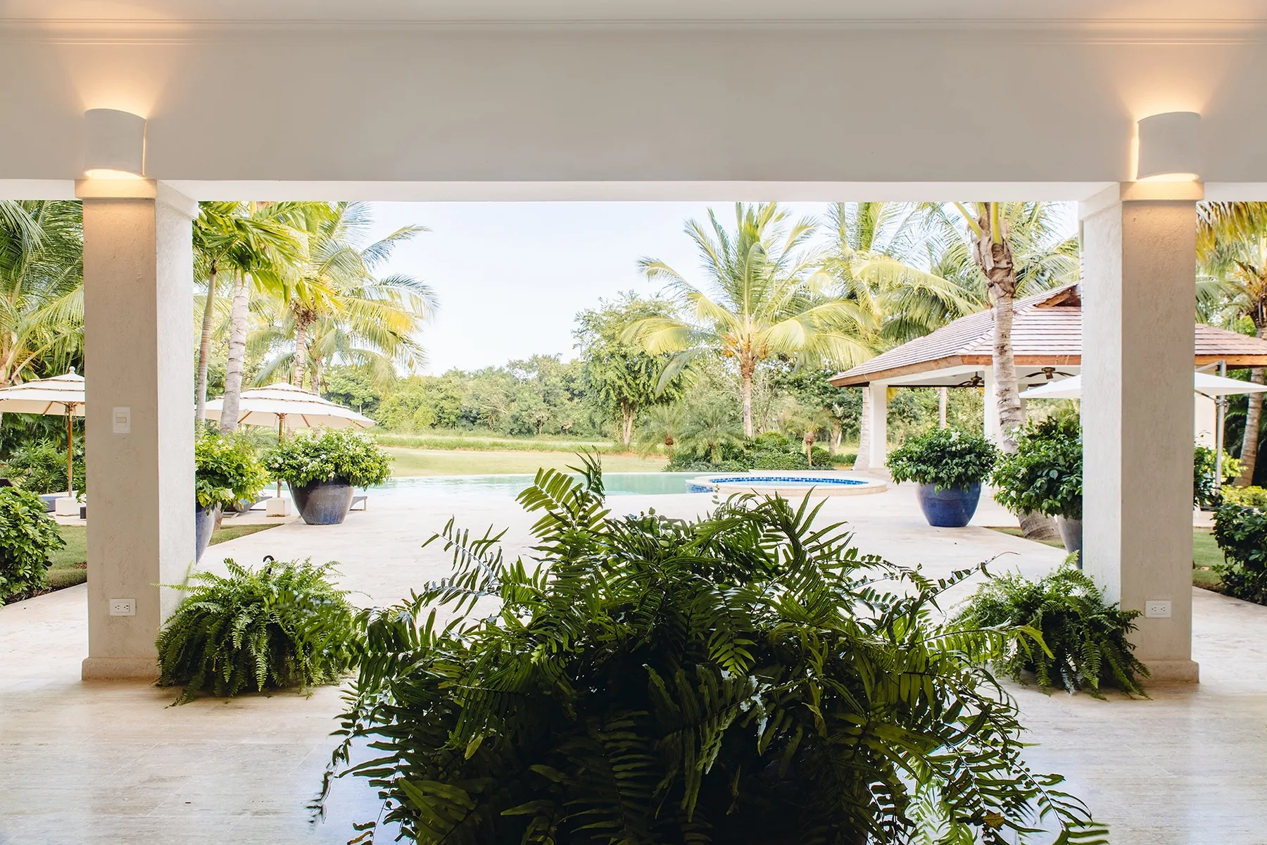 Un patio cubierto da a un jardín con piscina y plantas tropicales.