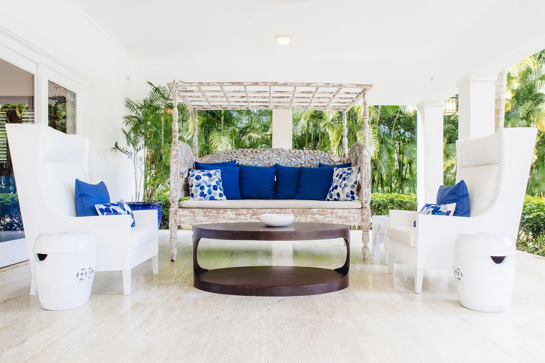 Una zona de estar exterior cubierta con cojines azules y abundante vegetación.