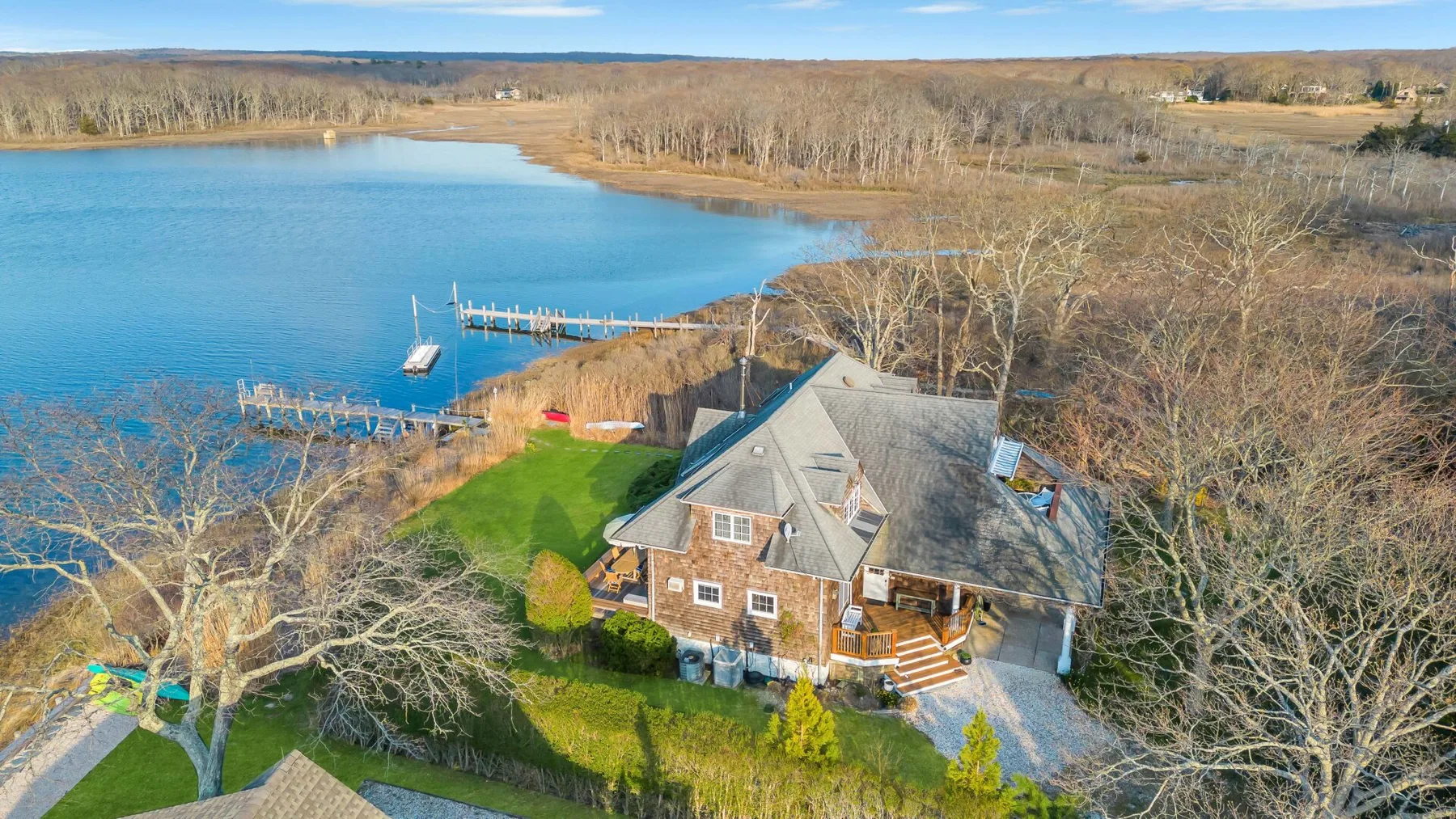 Una casa junto a un lago, con un muelle y césped verde.