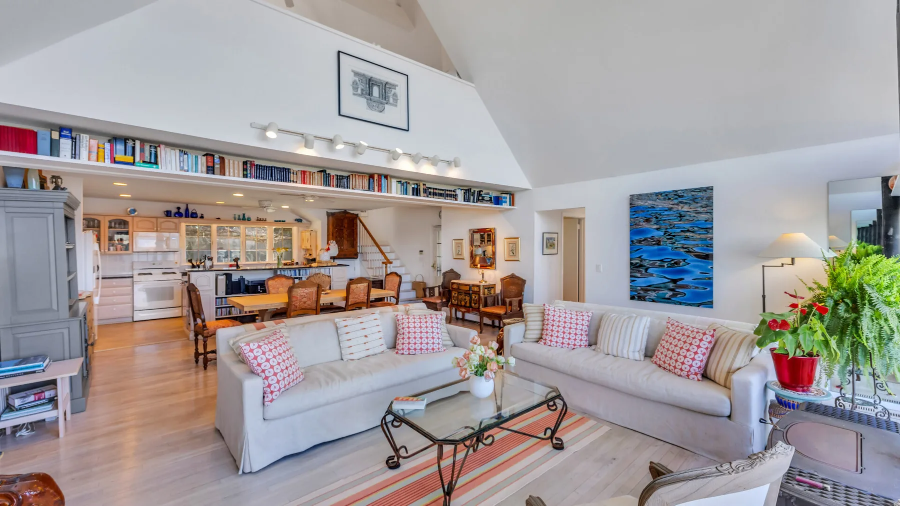 A bright open-plan living room with sofas, a dining table, and bookshelves.