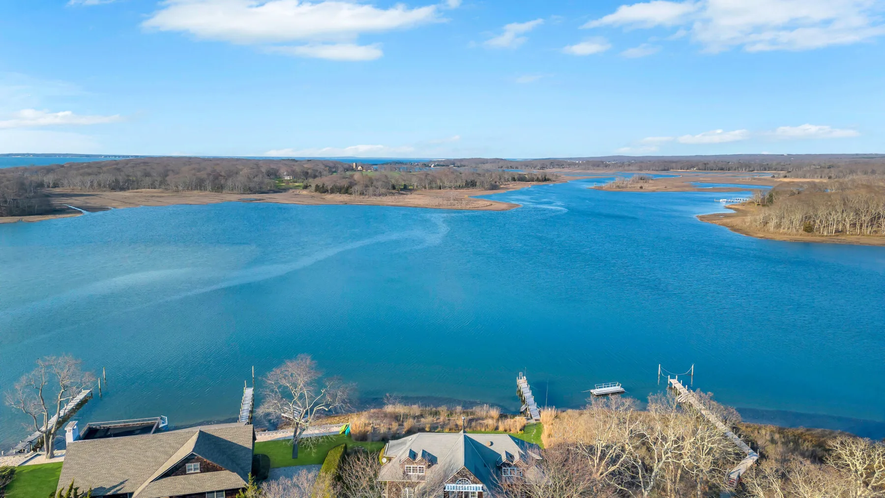 Aerial view of a blue lake with a few buildings along the wooded shoreline.
