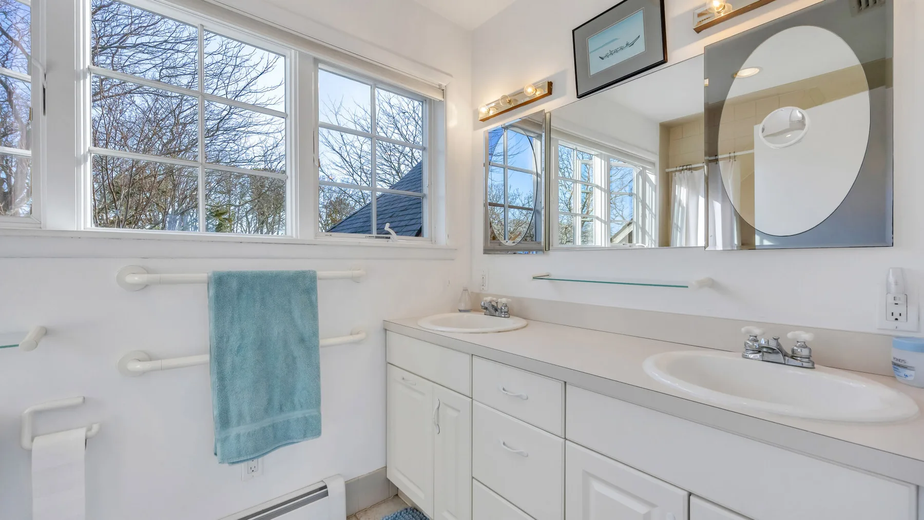 A bright bathroom with a wide vanity beneath a large mirror and windows.