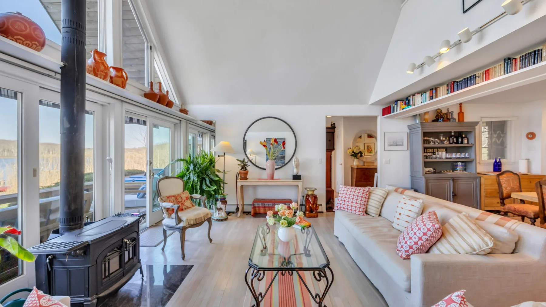 A bright living room with a long sofa, glass coffee table, and wood stove.