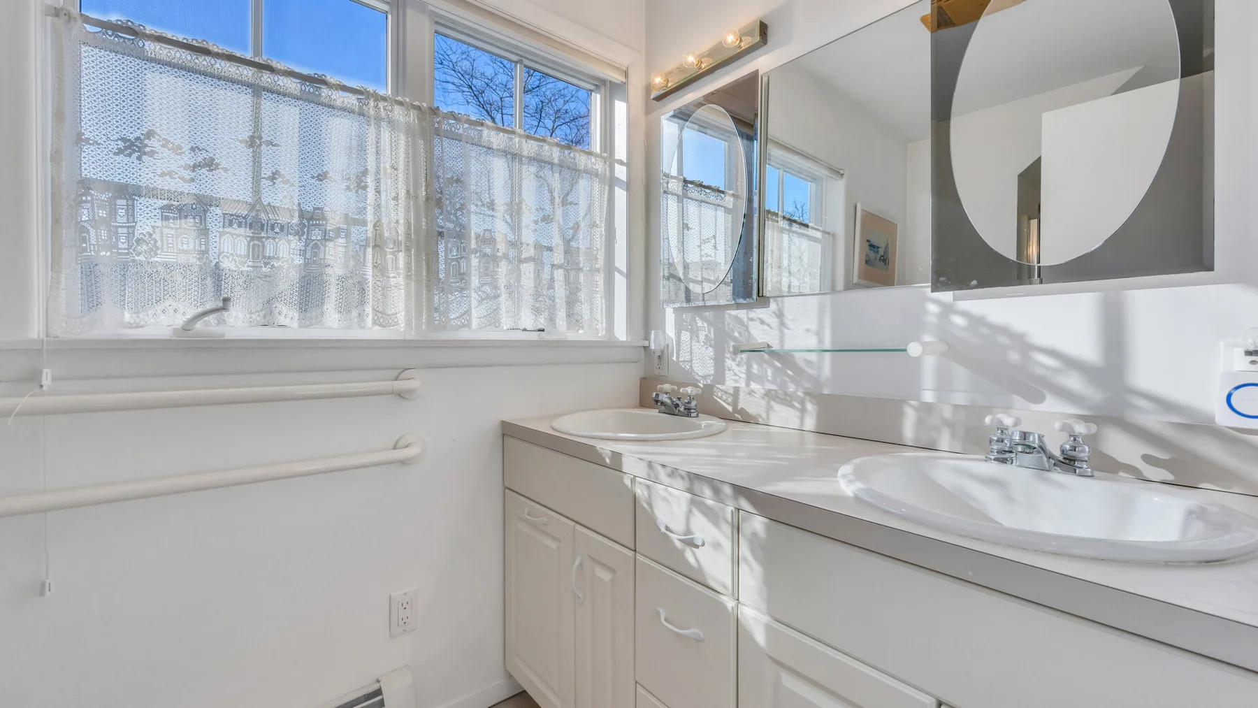 A bright bathroom with a long vanity, sink, and large windows.