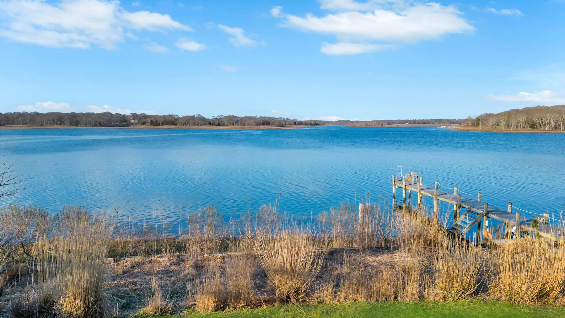 A broad blue lake meets a grassy shoreline beneath a partly cloudy sky.