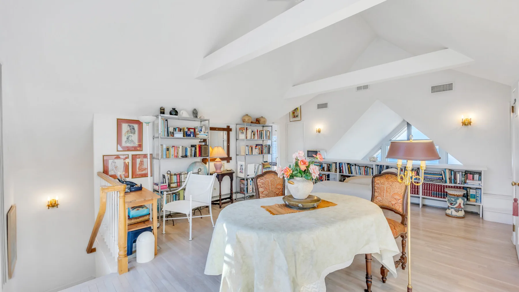 A bright attic living area with bookshelves and seating around a table.