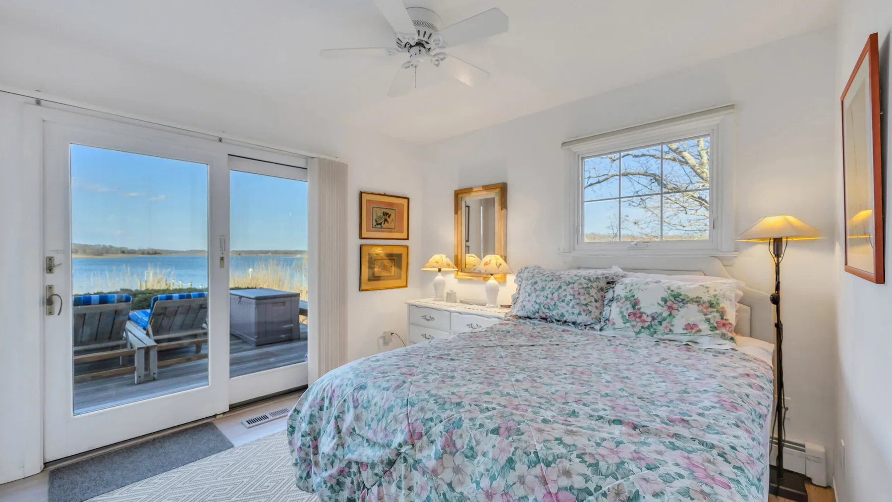 A bright bedroom with floral bedding and glass doors opening onto a waterfront view.