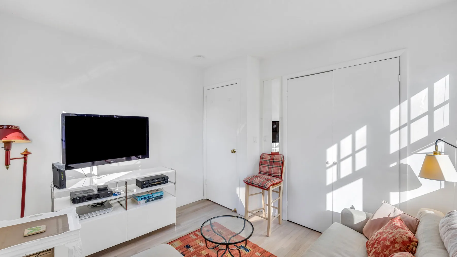 A bright living room with a television, seating, and sunlight across the floor.