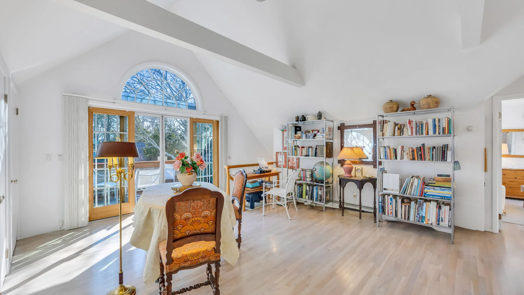 A bright living room with a dining table, bookshelves, and tall windows.