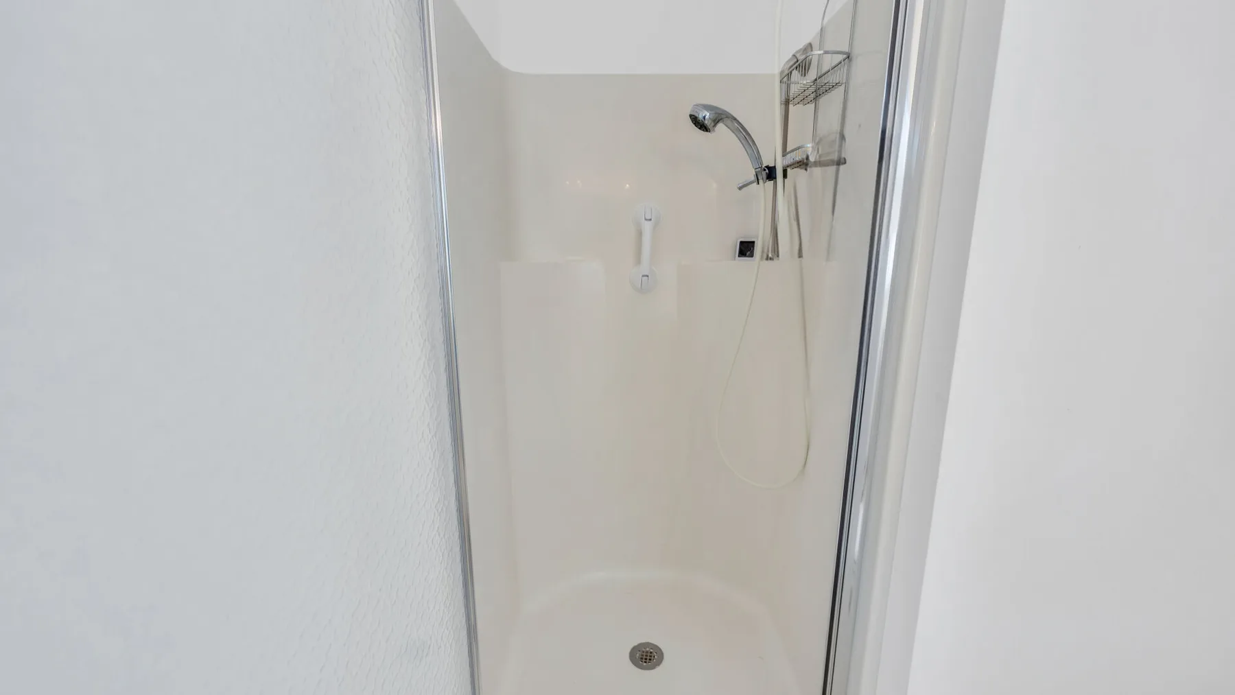 A bright bathroom shower with a handheld showerhead and drain.