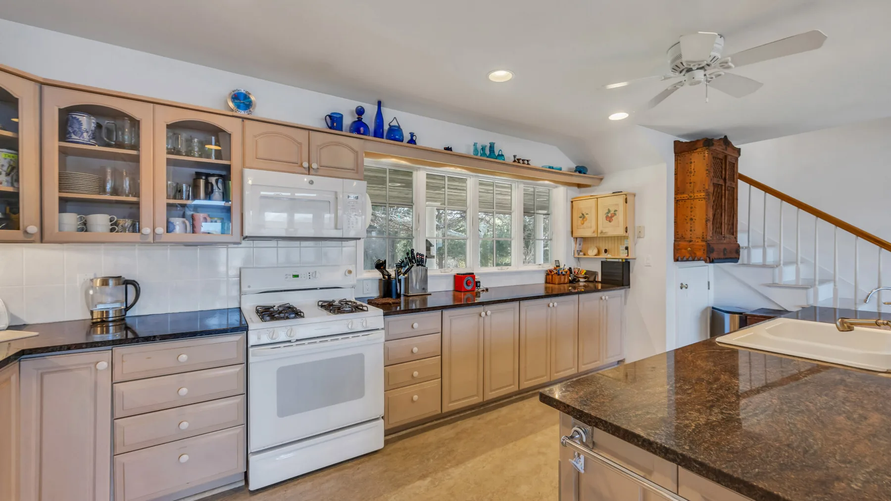 A spacious kitchen with wooden cabinets, a white stove, and a dark island countertop.
